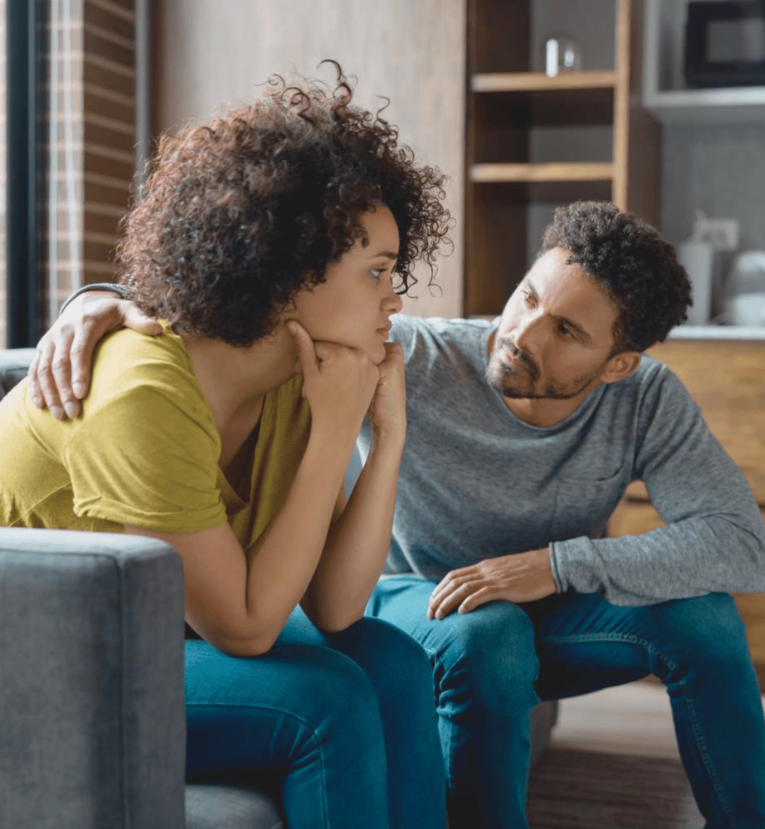A man and woman sitting on a couch, looking at each other seriously as they have an important conversation.