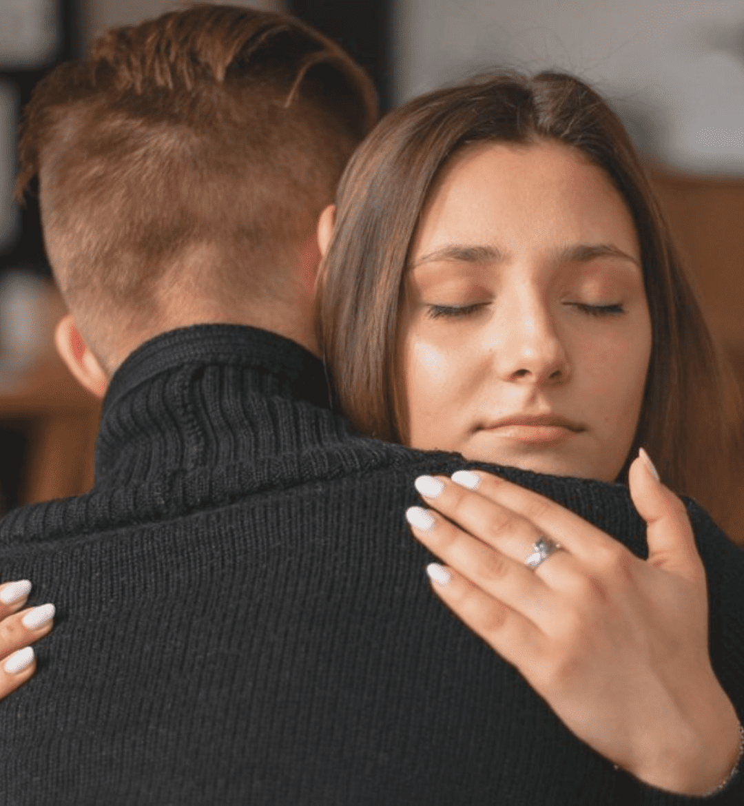 A woman with her eyes closed hugging a man in a black sweater, conveying deep emotion and connection.