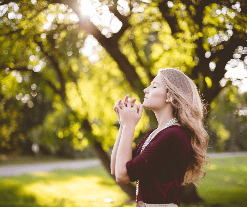 Woman praying outdoors in sunlight.