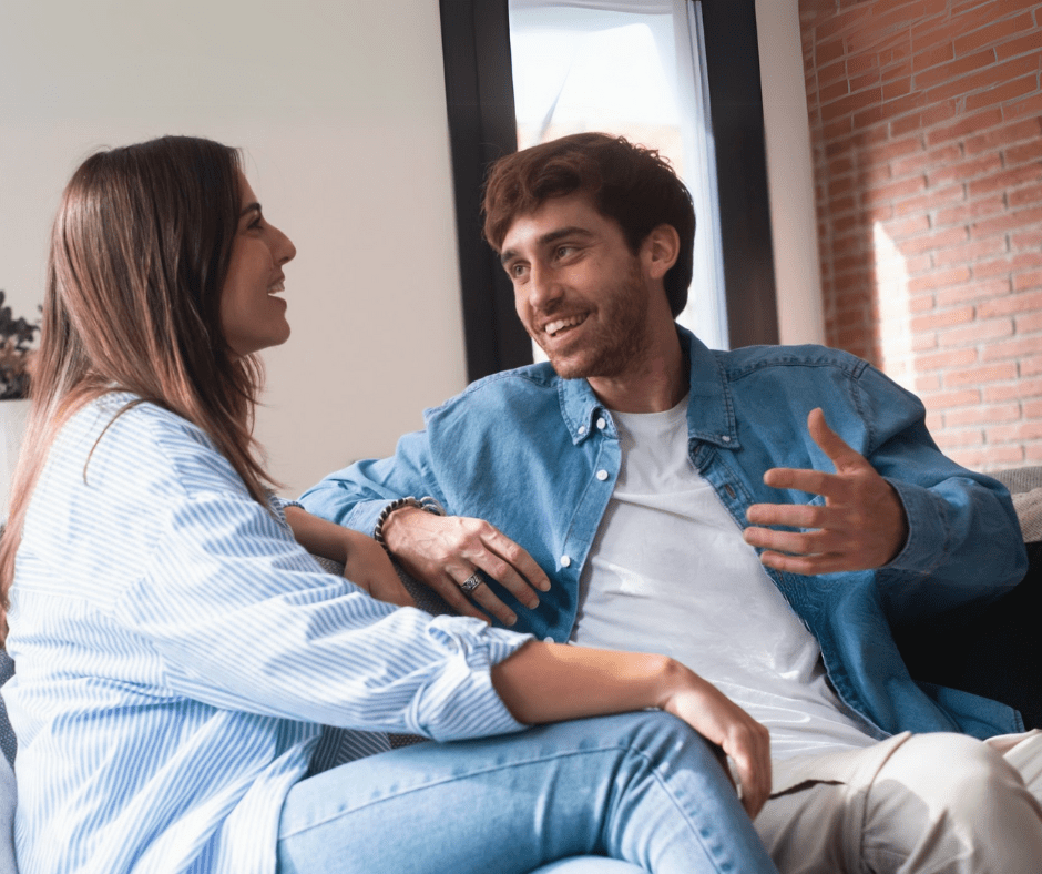 A man in a denim jacket talking animatedly with a woman in a striped shirt, both smiling and engaged in conversation.