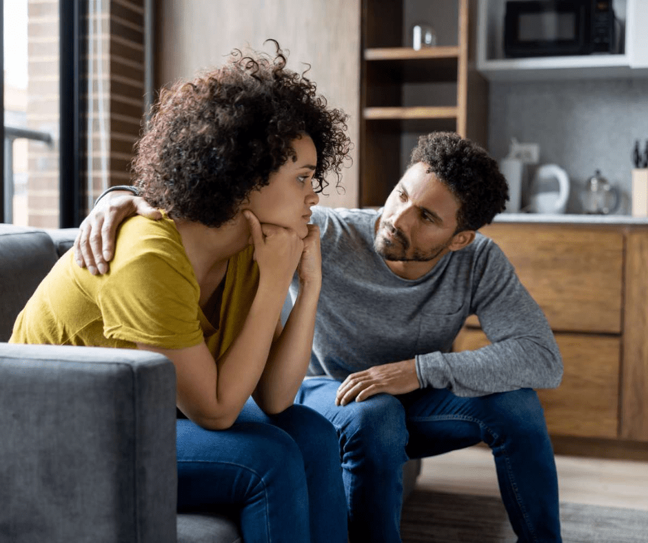 A man and woman sitting on a couch, looking at each other seriously as they have an important conversation.