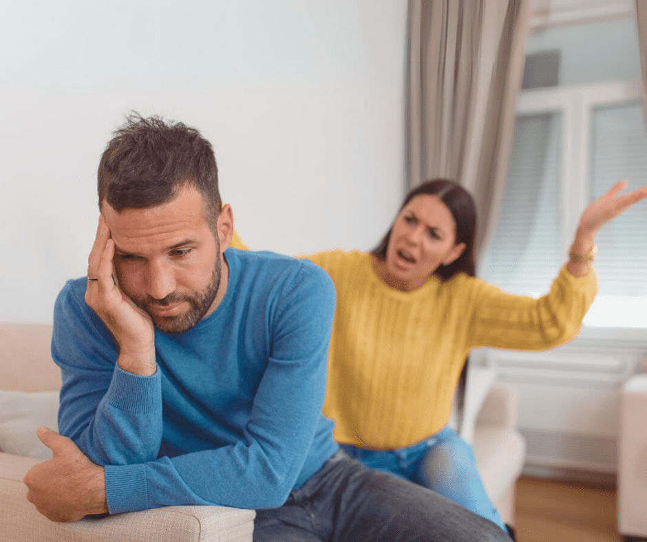 A frustrated woman gestures emotionally while her distant partner sits on the couch, avoiding eye contact