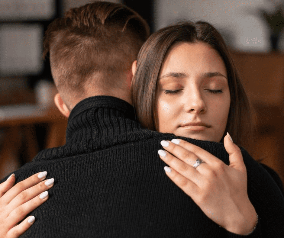 A woman with her eyes closed hugging a man in a black sweater, conveying deep emotion and connection.