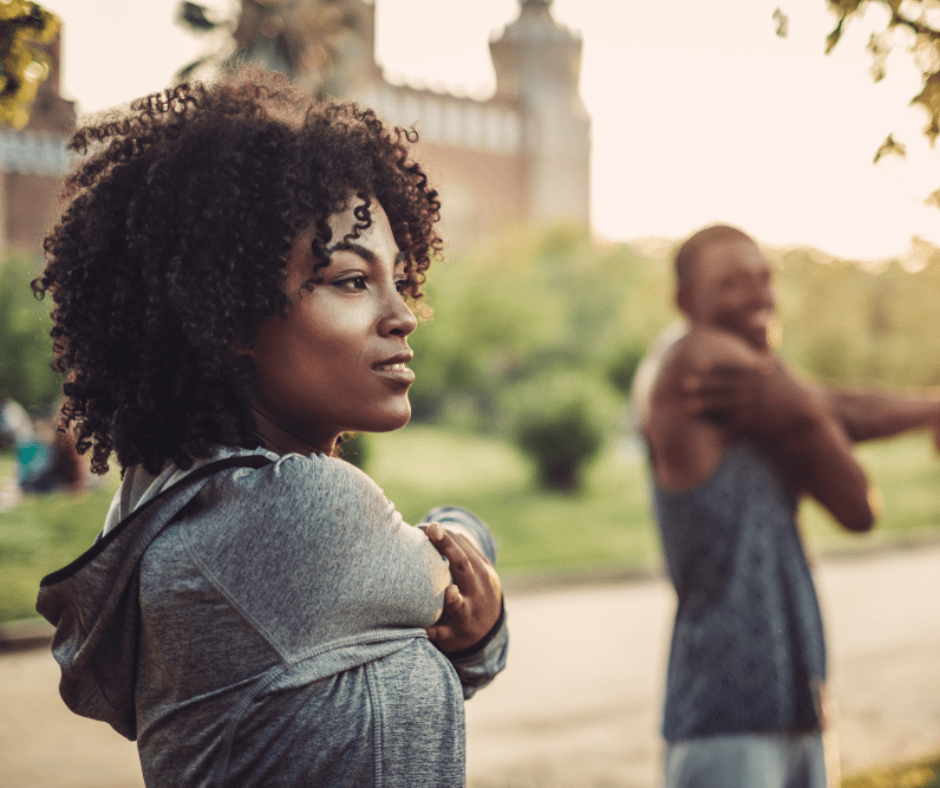 Fit woman stretching her arms in an outdoor park setting, showing determination and focus before exercise