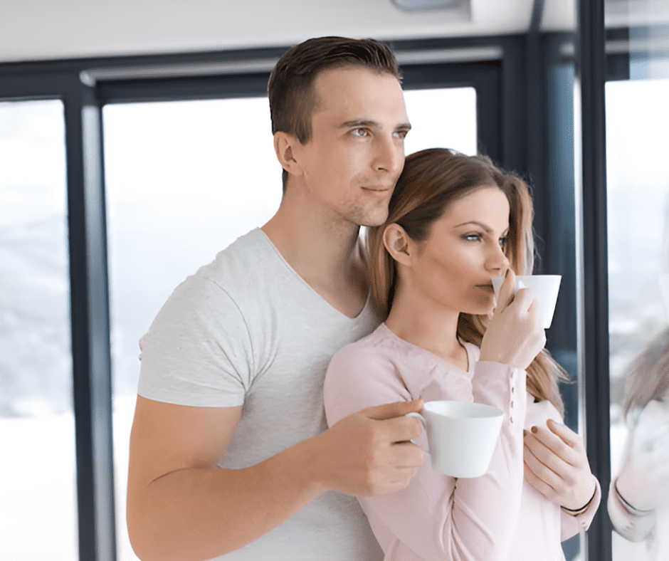 A young couple enjoying a quiet moment together while drinking coffee by a large window with a scenic view