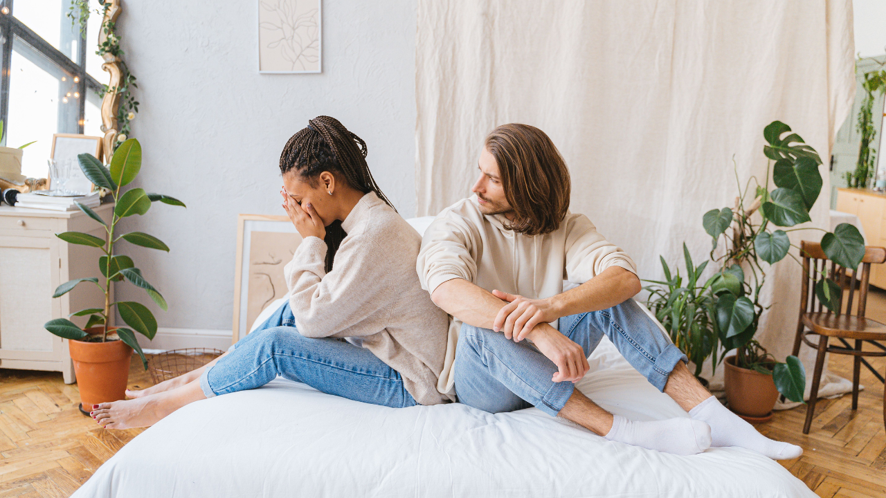 Couple sitting apart on a bed after an argument, showing emotional disconnection